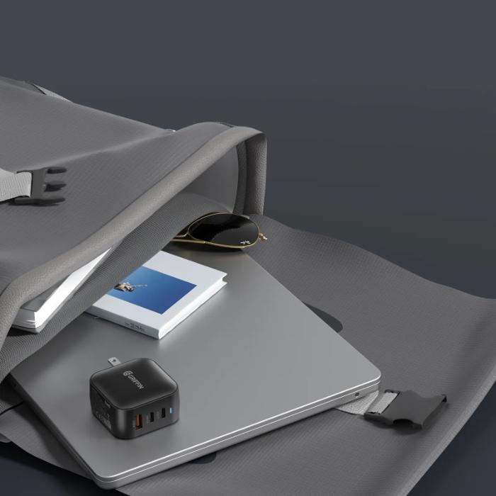 Laptop on a gray surface with a Black GRIFFIN PowerBlock 70w GaN PD3.0 Fast Charging Wall Charger, book, laptop and sunglasses.