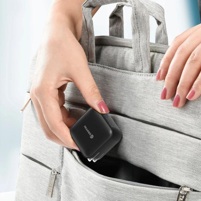 Person placing a Black GRIFFIN PowerBlock 100w GaN PD3.0 Fast Charging Wall Charger into a gray bag against a light blue background