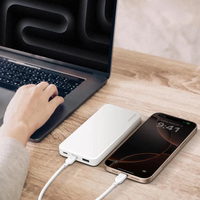 Person using a laptop with a White Momax IP155W 10000mAh 1-Power Vital Battery Pack and smartphone on a wooden desk.