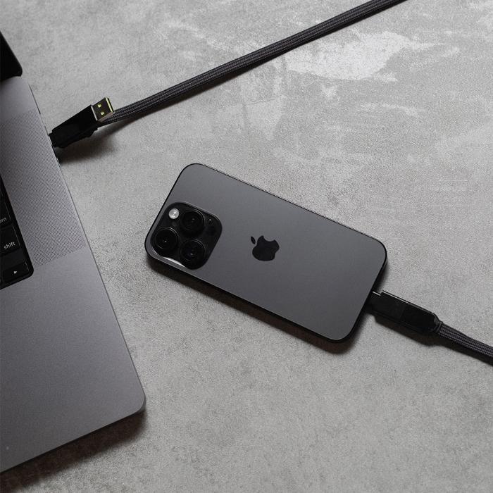 Black smartphone connected to a Black Rolling Square InCharge XL  6 in 1 100w Fast Charging and Data Cable  next to a laptop.