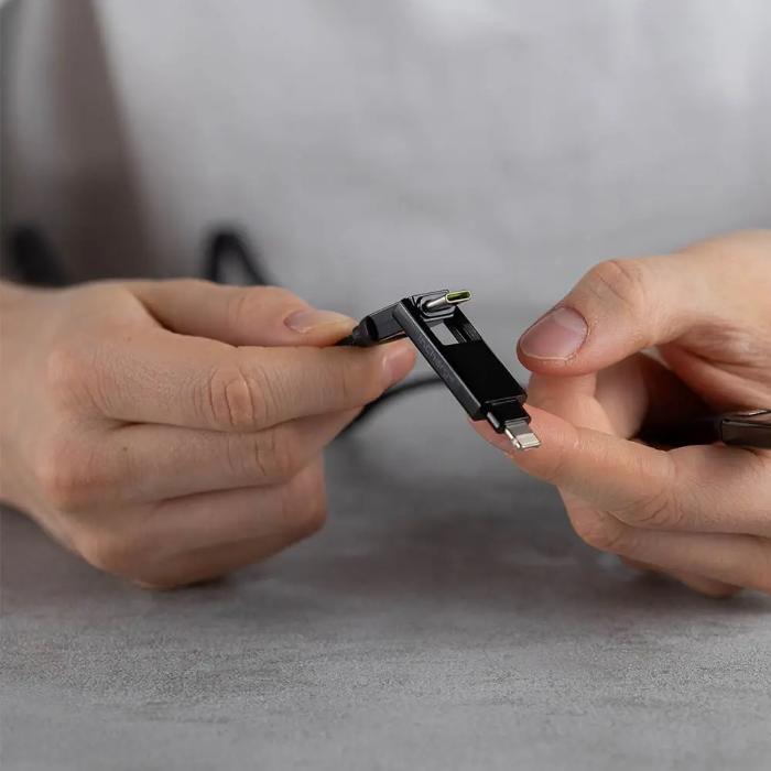 Close-up of hands holding a Black Rolling Square InCharge XL  6 in 1 KeyRing Size 100w Fast Charging and Data Cable on a gray background